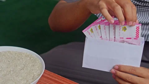 Close-up of hands preparing cash and rice for Islamic Zakat Fitrah charity Stock Footage 328987097