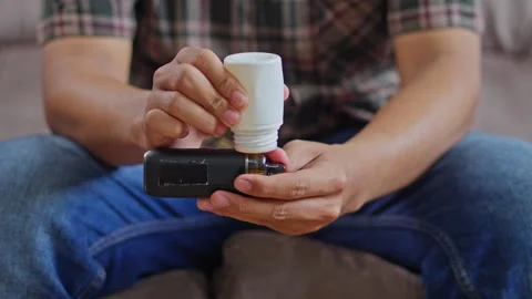 Close-up of Hands preparing an electronic vaping device by refilling cartridge Stock Footage 332389033