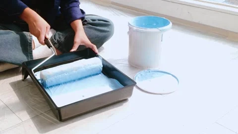 Close-up of hands preparing a paint roller with blue paint from a tray. Stock Footage 313587334
