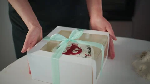 Close-up of hands presenting a gift cake wrapped in a box with a bow Stock Footage 336049452