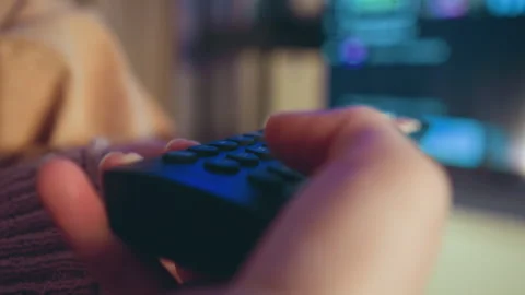 Close-up hands pressing buttons on remote control in cozy living room with warm Stock-Footage 345656015