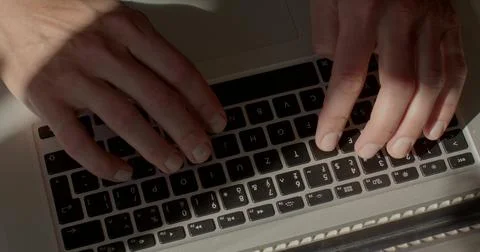 Close-up of hands pressing keyboard black buttons on grey laptop in sunny. Stock Photos