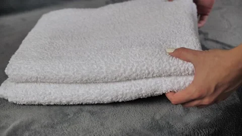 Close-up of hands putting stack of fresh white bath towels on the bed sheet Stock Footage 140762433
