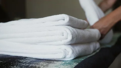 Close-up of hands putting stack of fresh white bath towels on the bed in hotel Stock Footage 221124719