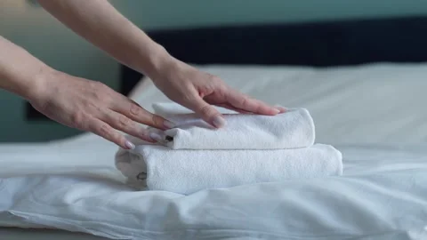 Close-up of hands putting stack of fresh white bath towels on the bed sheet Stock Footage 252660313
