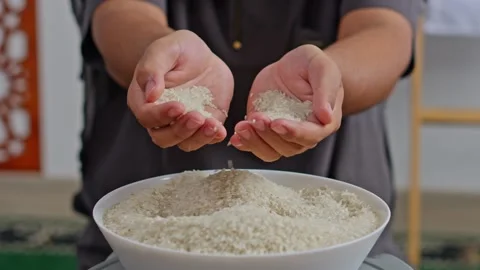 Close-up of hands releasing rice grains into bowl for Zakat al-Fitr or food Stock Footage 329103166