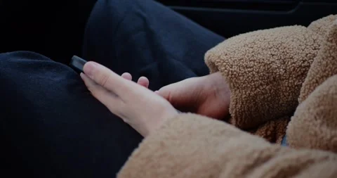 Close-up of hands resting in lap, holding a smartphone, wearing a cozy... Stockbeeldmateriaal 319881975
