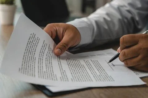 Close-up of hands reviewing printed documents and signing on a marked line .. Foto stock
