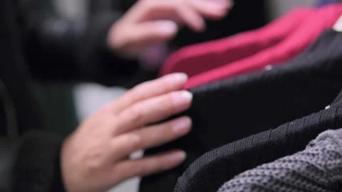 Close-up of hands rotating a clothing rack with hangers in a store, focusing on Stock Footage 295930428