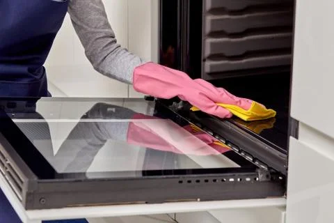Close-up of hands in rubber gloves with a microfiber cloth washing the oven. Stock Photos
