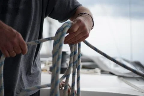 Close up of hands of a sailor man coiling up a rope, the halyard on a sailboat Foto stock