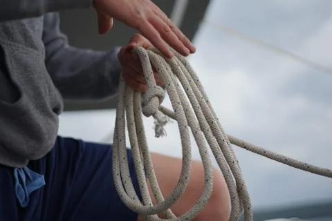 Close up of hands of a sailor man coiling up a rope, the halyard on a sailboat Stock Photos