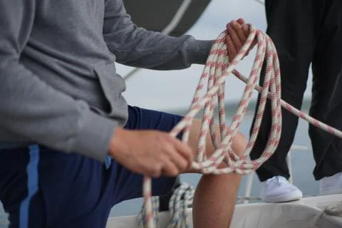 Close up of hands of a sailor man coiling up a rope, the halyard on a sailboat Stock Photos
