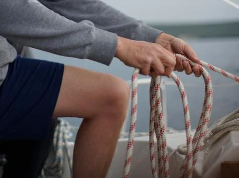 Close up of hands of a sailor man coiling up a rope, the halyard on a sailboat Foto stock