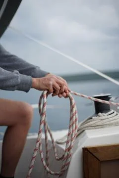 Close up of hands of a sailor man coiling up a rope, the halyard on a sailboat Stock Photos