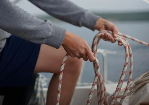 Close up of hands of a sailor man coiling up a rope, the halyard on a sailboat Stock Photos