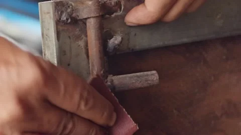 Close-up of hands sanding a rusty metal door hinge with sandpaper for home .. Stockbeeldmateriaal 338225395