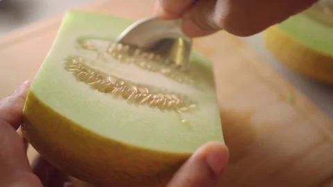 Close-up of Hands Scooping Seeds from a Fresh Honeydew Melon Half Stock Footage 334765169
