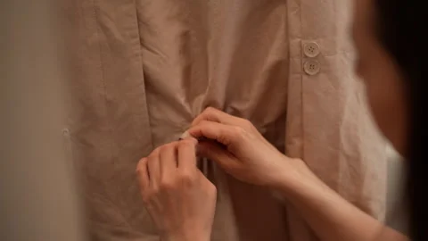 Close-up hands of seamstress adjusting drawstring on back of beige garment Stock Footage 310625405