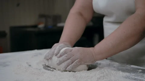 Close-up of hands of senior bakery chef applying flour to dough, kneading dough Stock Footage 140234122