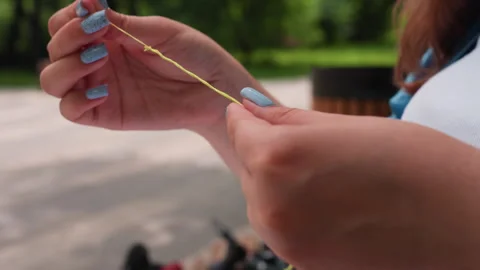 Close Up Hands Separating Green Thread Outdoors with Blurred Park Background Stock Footage 322668660
