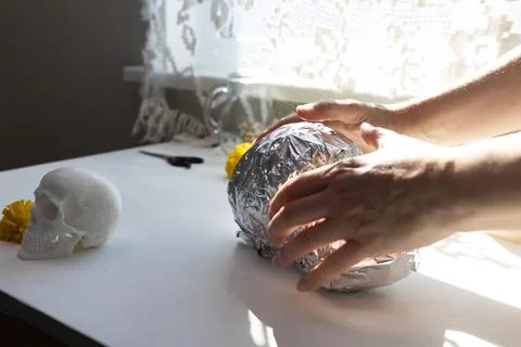 Close-up of hands shaping a foil-wrapped sphere beside a white skull model at Stock Photos