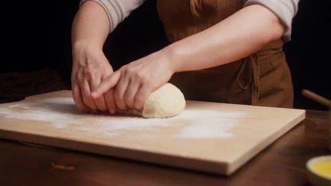 Close-up of hands shaping soft bread dough into a smooth round loaf on a floured Stock Footage 340564194