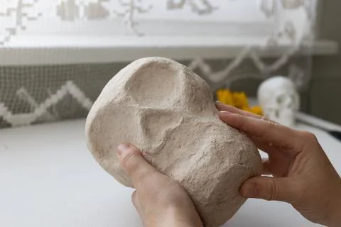 Close-up of hands shaping a textured plaster skull in progress in a bright in Stock Photos