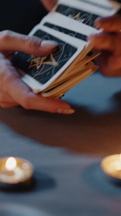 Close-up of hands shuffling tarot cards with burning candles on table Vídeos de archivo 316877447
