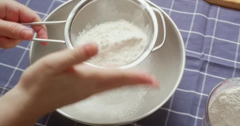 Close up of hands sifting flour through a sieve in the kitchen preparing Stock Footage 319383720