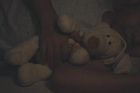Close-up of the hands of a sleeping boy from the dark embrace a teddy bear. s Stock Photos