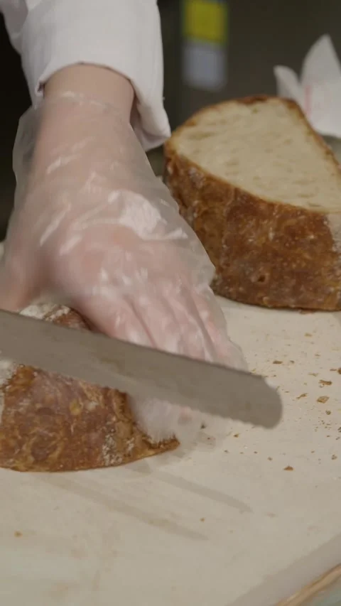 Close-up of Hands Slicing Fresh Artisan Bread on a Cutting Board Stock Footage 335975020