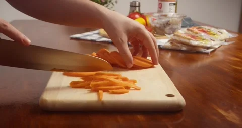 Close up of hands slicing fresh carrot into thin strips with a kitchen knife on Stock-Footage 335813459