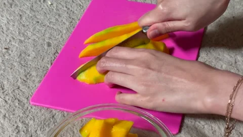Close up of hands slicing a fresh ripe mango on a pink cutting board. Stock Footage 325451758