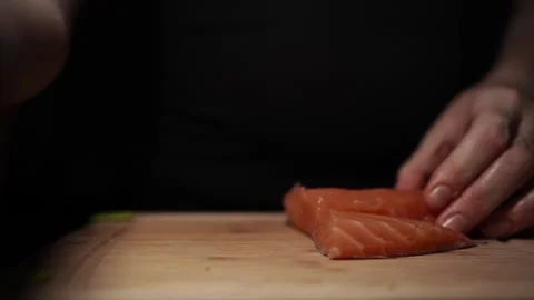 Close-Up of Hands Slicing Fresh Salmon Fillet on a Dark Background Stock-Footage 303895413
