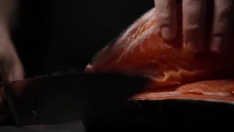 Close-Up of Hands Slicing Fresh Salmon Fillet on a Dark Background Video stock 303895653