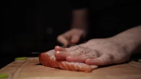 Close-Up of Hands Slicing Fresh Salmon Fillet on a Dark Background Stockbeeldmateriaal 303900778