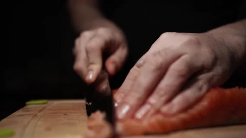 Close-Up of Hands Slicing Fresh Salmon Fillet on a Dark Background Видео 303900826