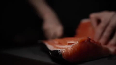 Close-Up of Hands Slicing Fresh Salmon Fillet on a Dark Background Stock Footage 303901587