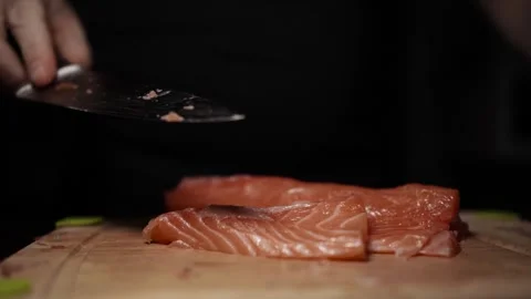 Close-Up of Hands Slicing Fresh Salmon Fillet on a Dark Background Video stock 303906184