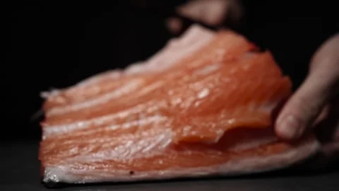 Close-Up of Hands Slicing Fresh Salmon Fillet on a Dark Background Video stock 303906272