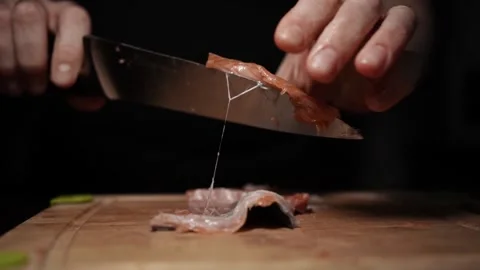 Close-Up of Hands Slicing Fresh Salmon Fillet on a Dark Background Stock Footage 303911573