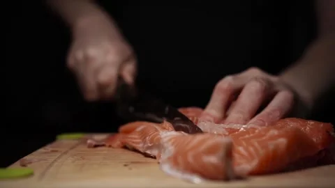 Close-Up of Hands Slicing Fresh Salmon Fillet on a Dark Background Stock Footage 303911697