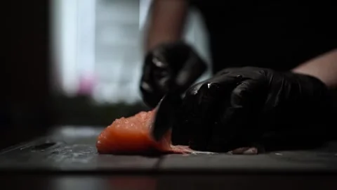 Close-Up of Hands Slicing Fresh Salmon Fillet on a Dark Background Stock Footage 303916336