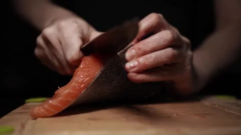 Close-Up of Hands Slicing Fresh Salmon Fillet on a Dark Background Video stock 303920539