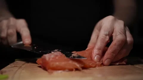 Close-Up of Hands Slicing Fresh Salmon Fillet on a Dark Background Stock Footage 303920685