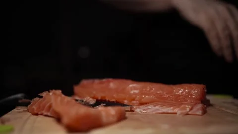 Close-Up of Hands Slicing Fresh Salmon Fillet on a Dark Background Video stock 303920731