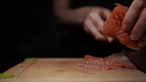 Close-Up of Hands Slicing Fresh Salmon Fillet on a Dark Background Video stock 303923743