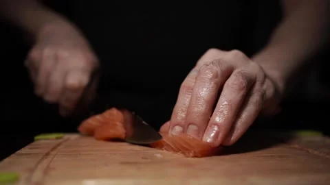 Close-Up of Hands Slicing Fresh Salmon Fillet on a Dark Background Stock Footage 303924820