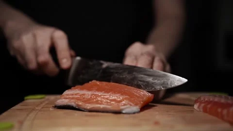 Close-Up of Hands Slicing Fresh Salmon Fillet on a Dark Background Vídeos de archivo 303925867